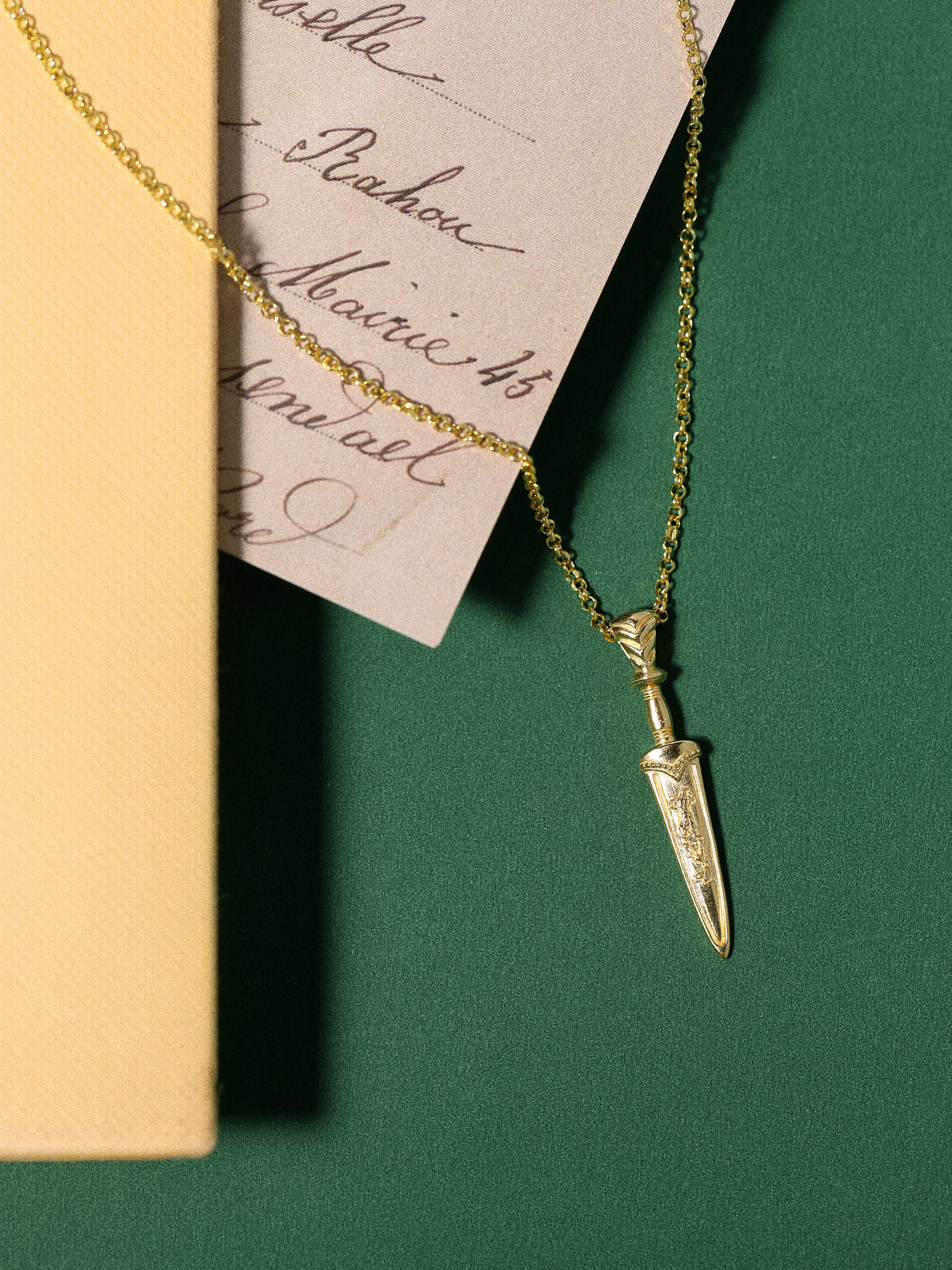 Gold necklace with a dagger pendant on a green surface