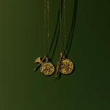 Two gold necklaces with pendants on a dark green background