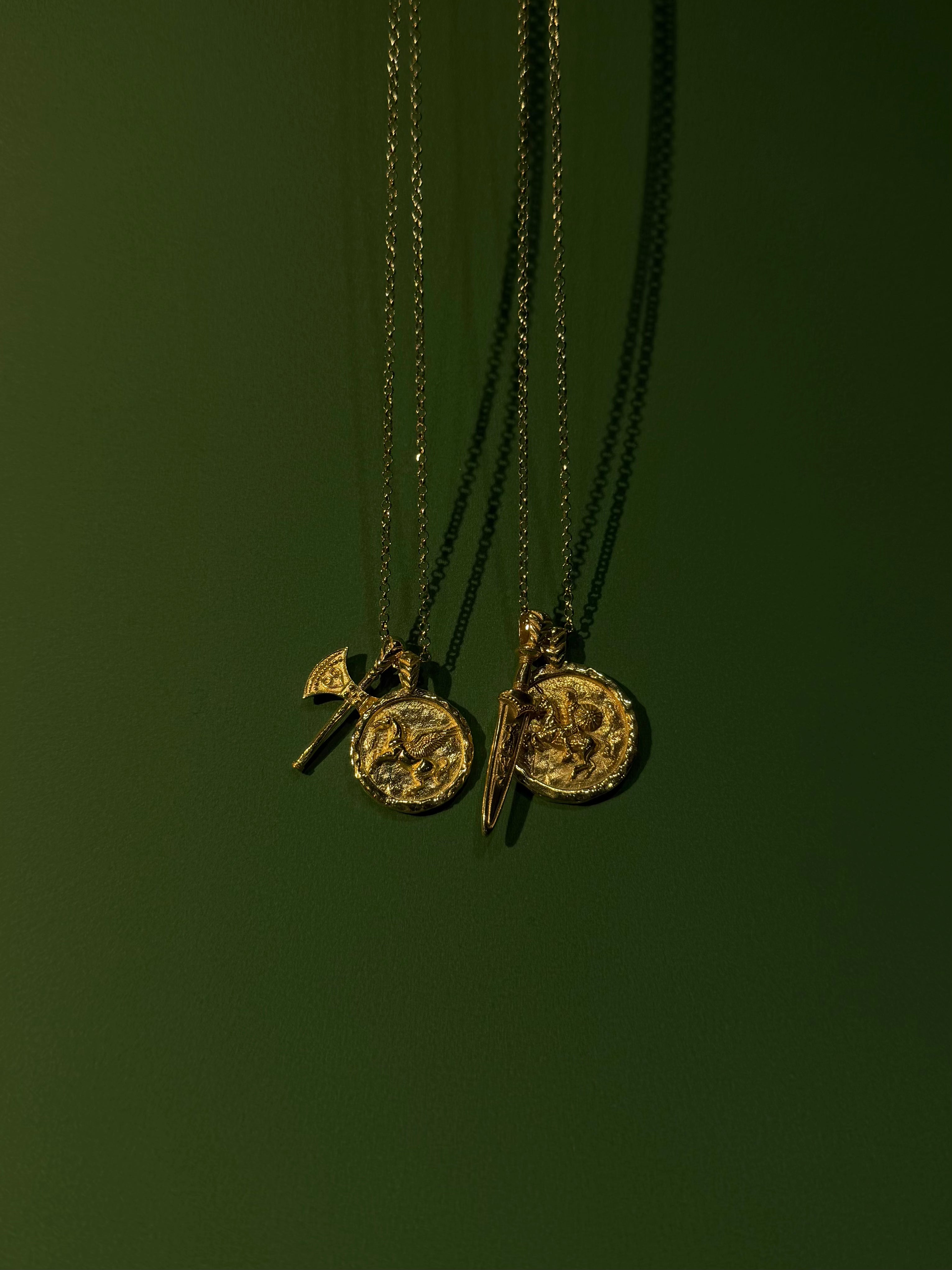 Two gold necklaces with pendants on a dark green background