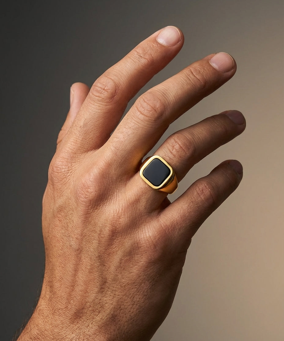 Hand wearing a gold ring with a black stone on a gradient background