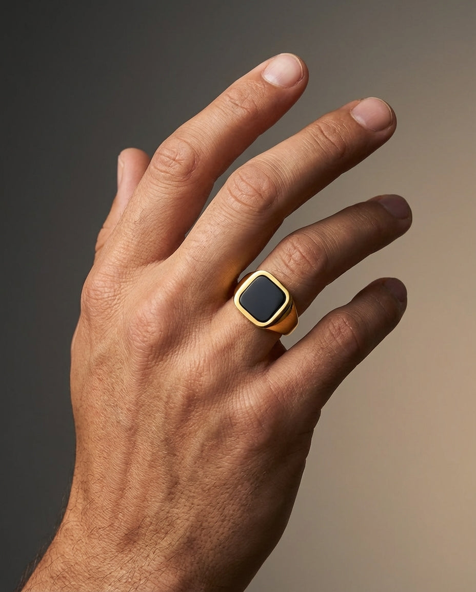 Hand wearing a gold ring with a black stone on a gradient background