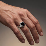 Hand wearing a silver ring with a black stone on a gradient background