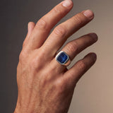 Hand wearing a ring with a blue gemstone on a gradient background