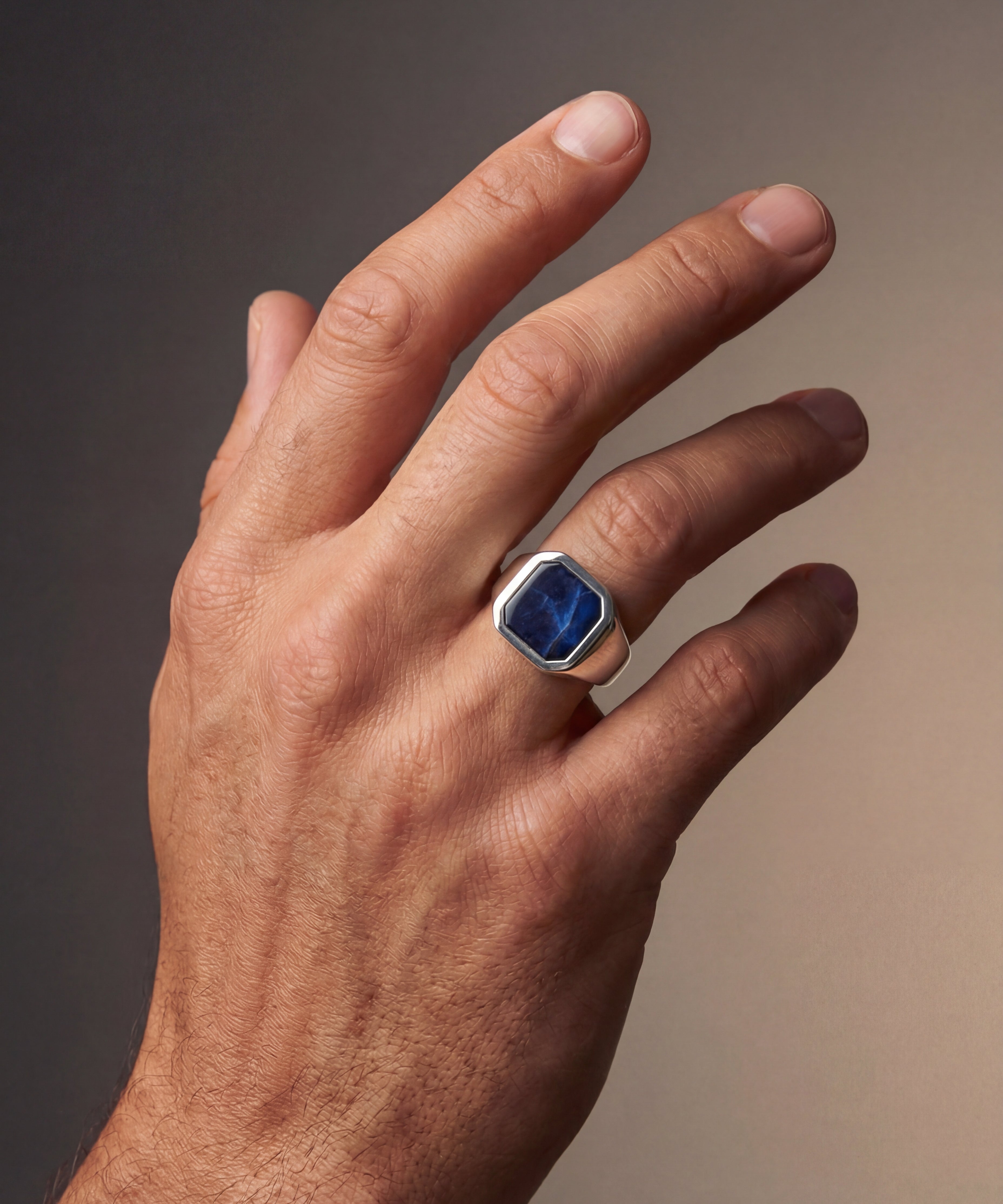 Hand wearing a ring with a blue gemstone on a gradient background