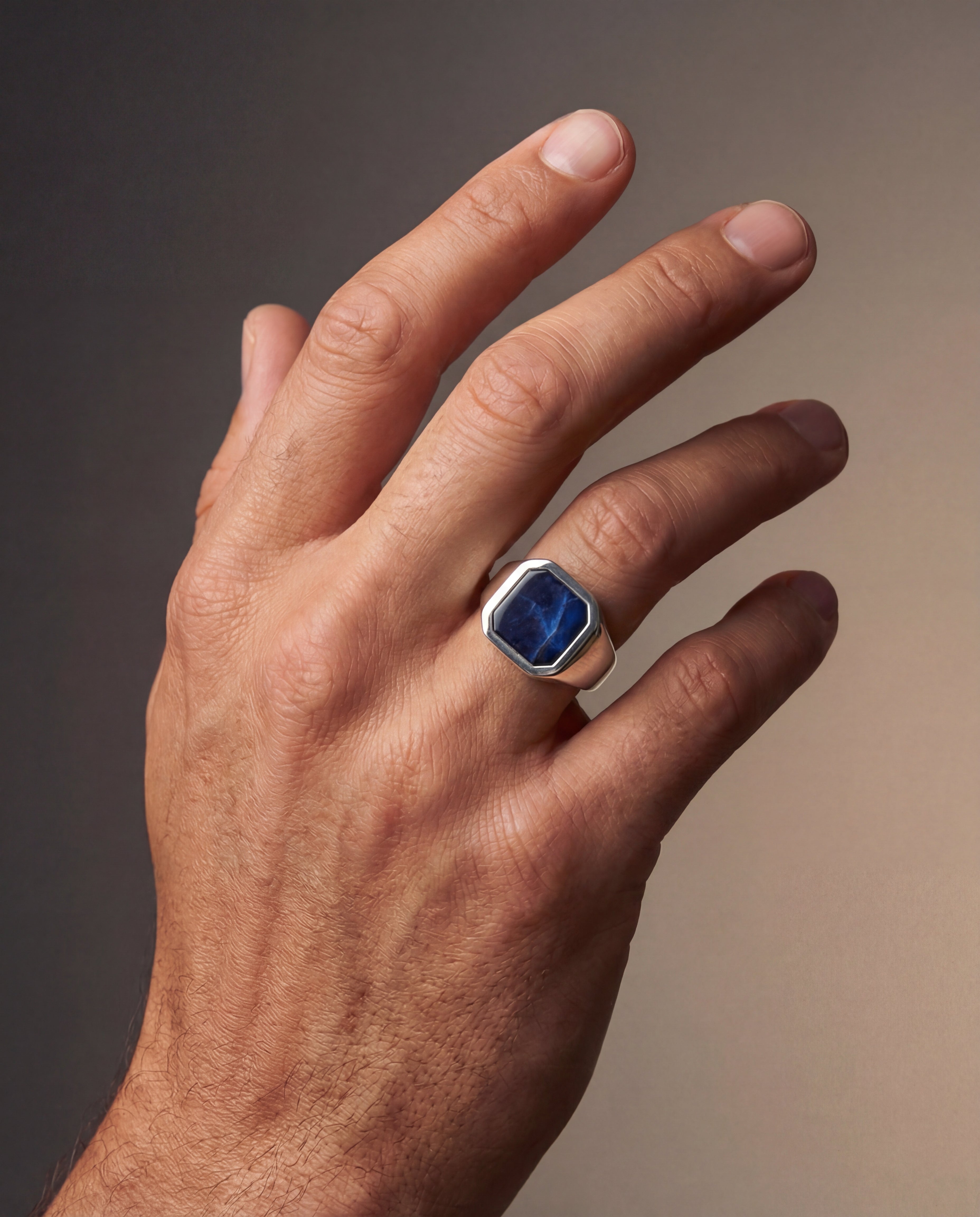 Hand wearing a ring with a blue gemstone on a gradient background