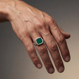 Hand wearing a green gemstone ring on a gradient background