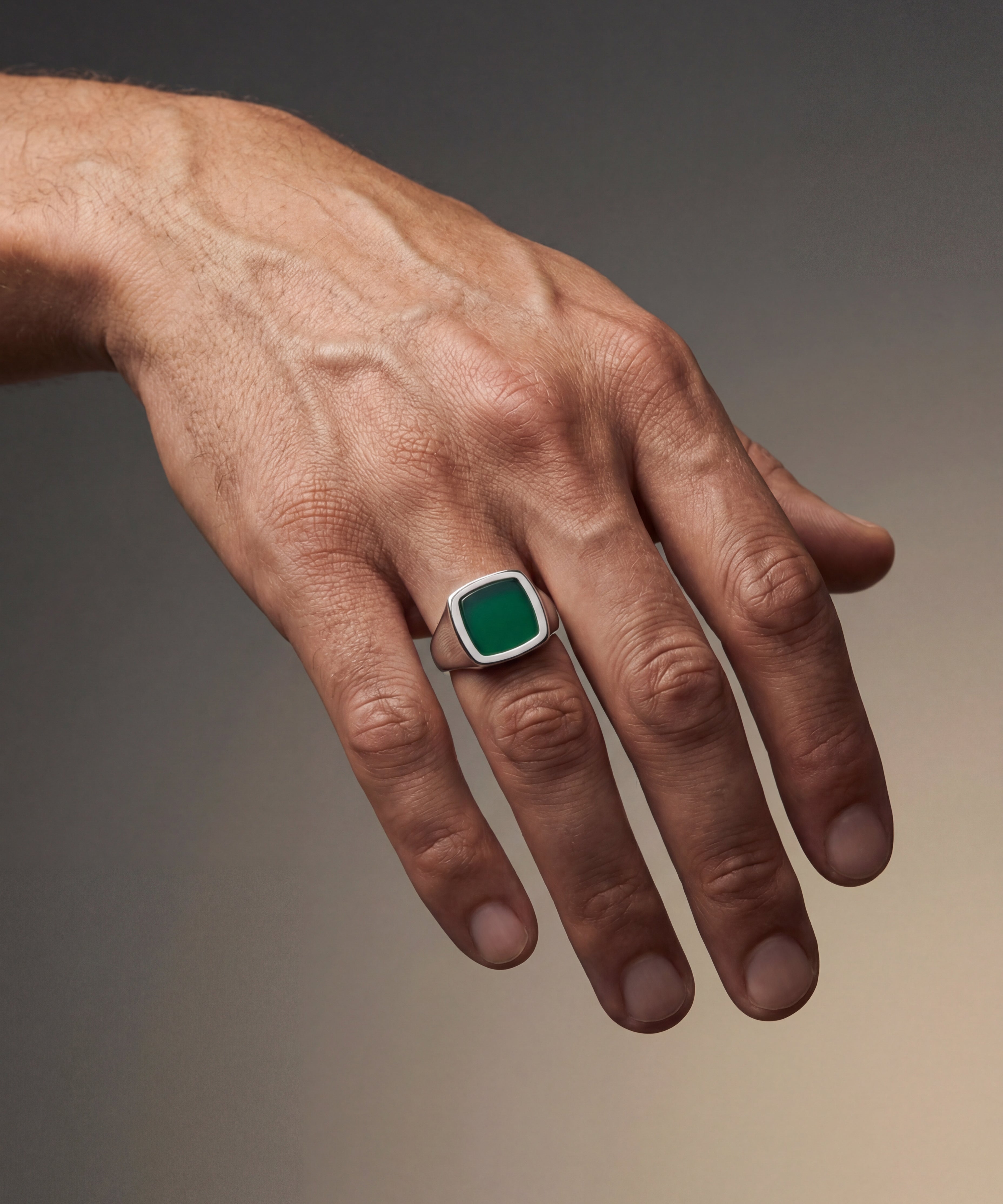 Hand wearing a green gemstone ring on a gradient background