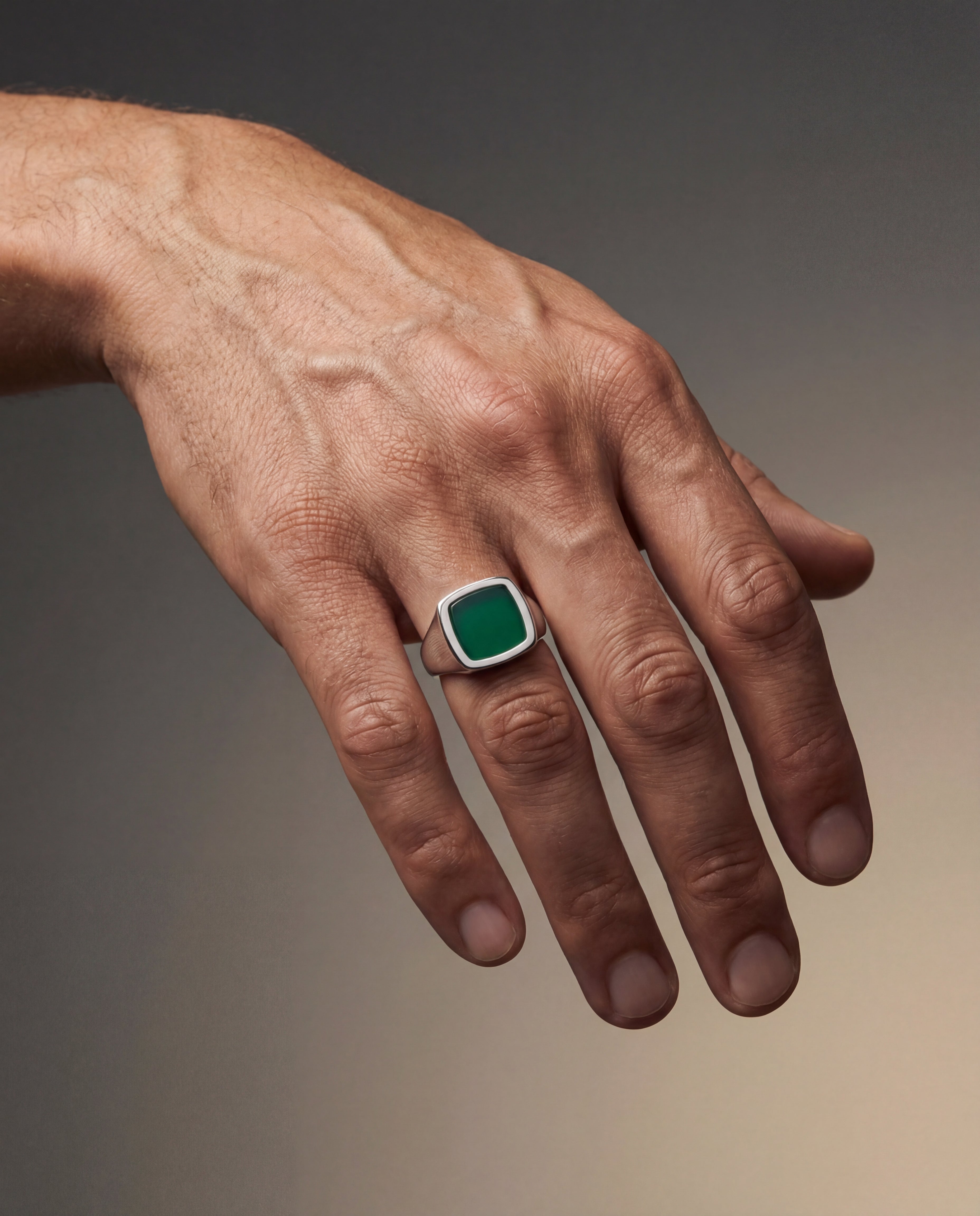 Hand wearing a green gemstone ring on a gradient background