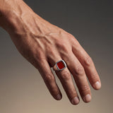 Hand wearing a ring with a red stone on a gradient background