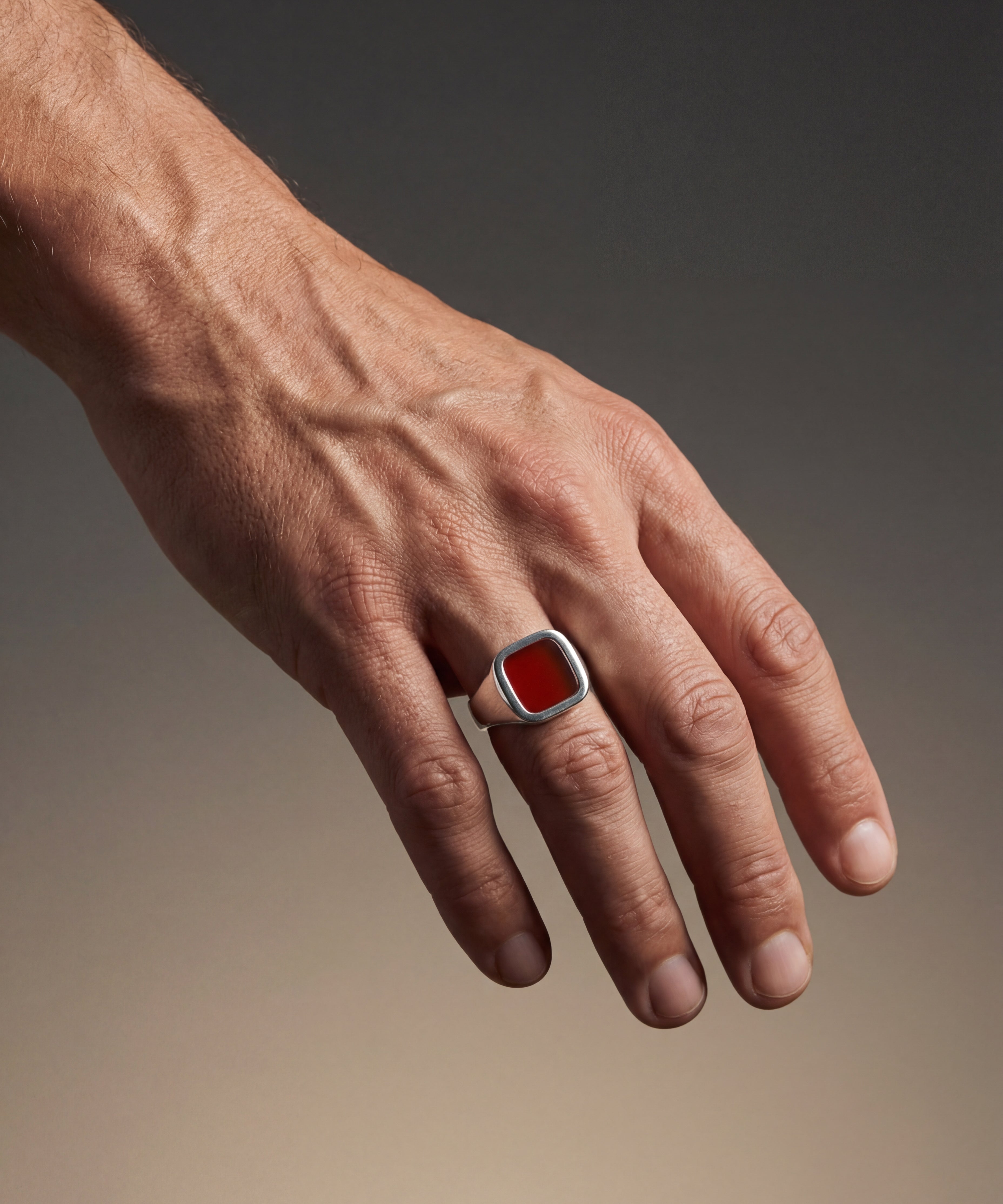 Hand wearing a ring with a red stone on a gradient background