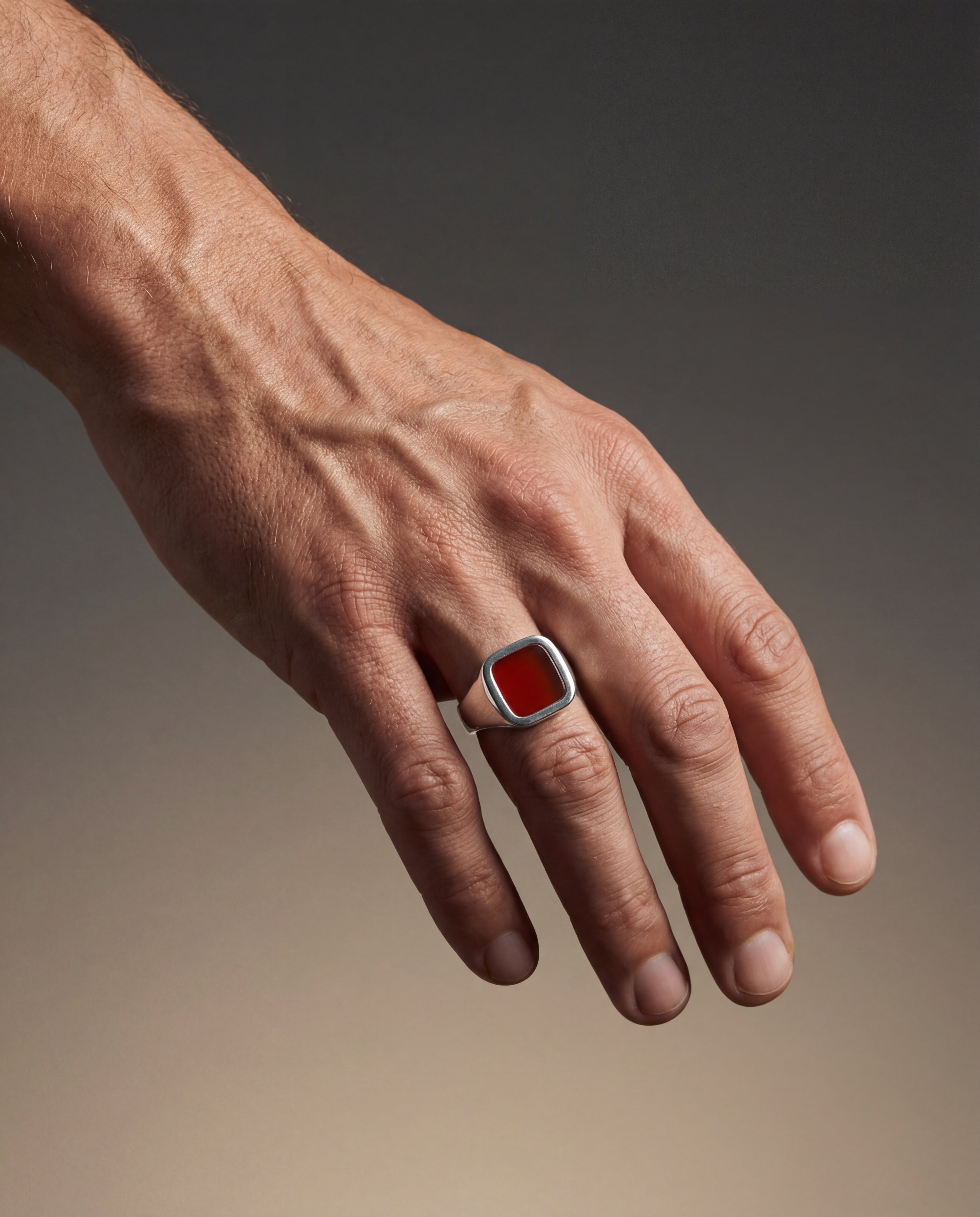 Hand wearing a ring with a red stone on a gradient background
