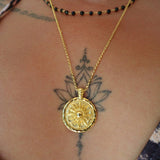Gold necklace with a round coin pendant on a person's neck with tattoos.