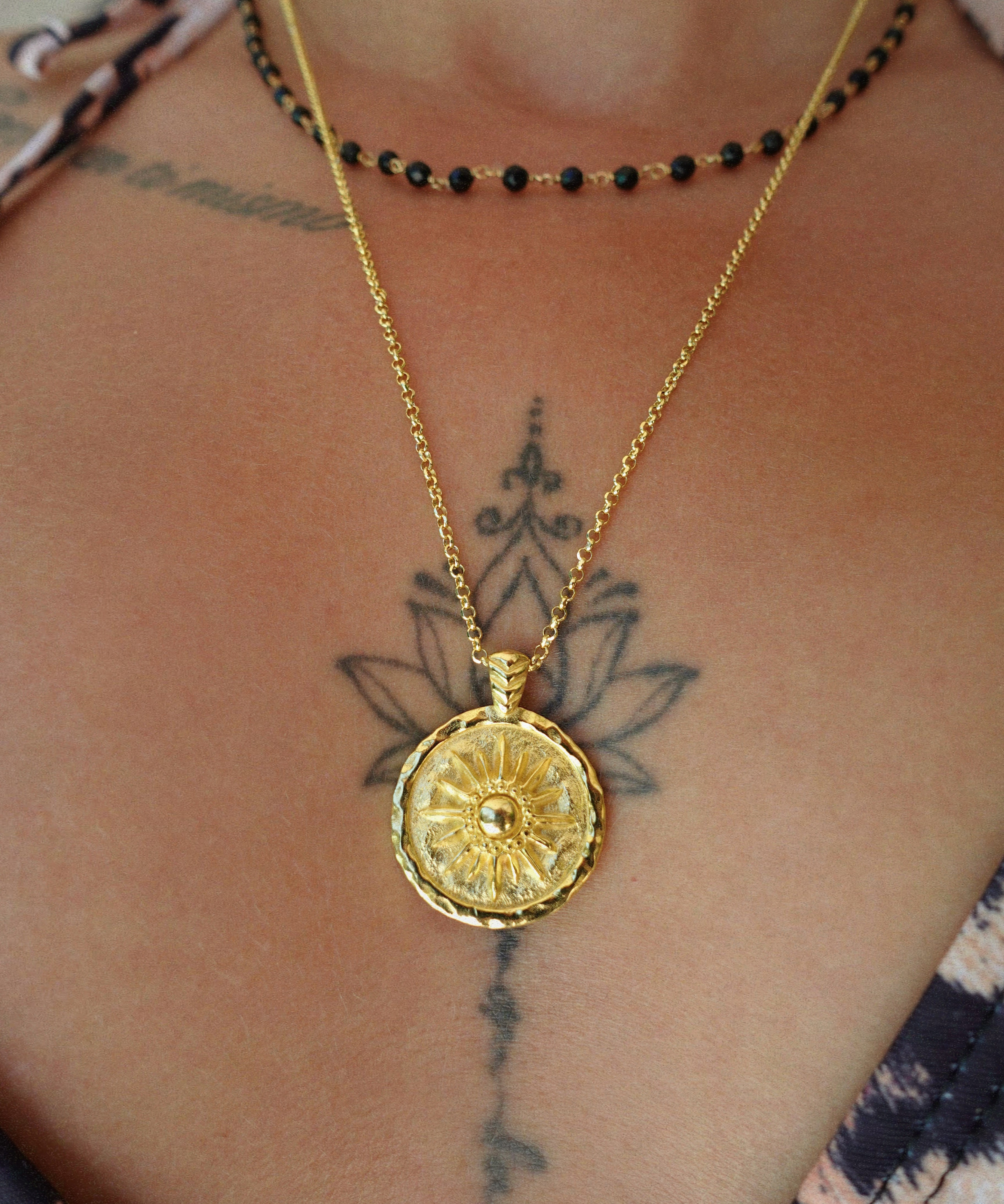 Gold necklace with a round coin pendant on a person's neck with tattoos.