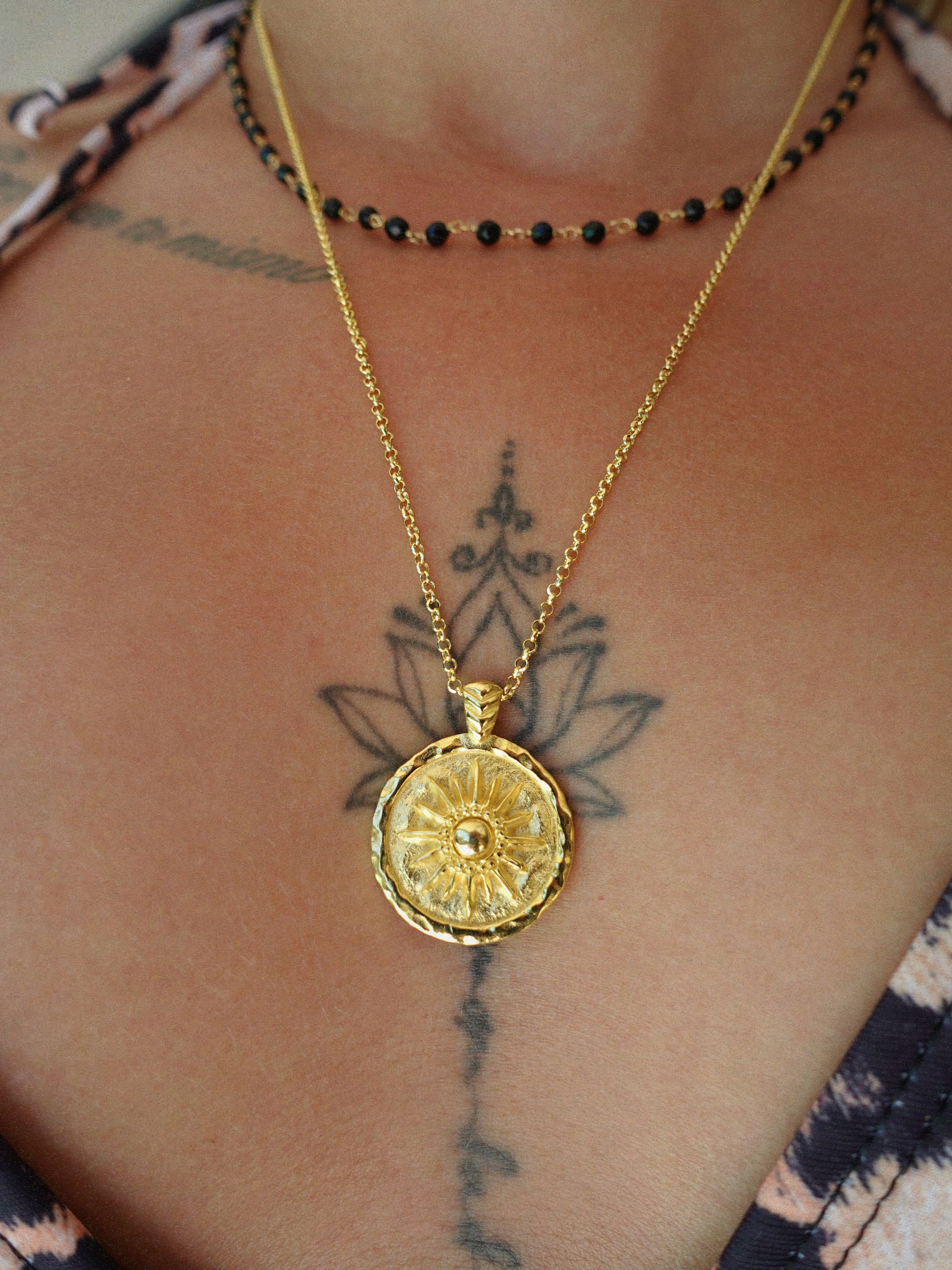 Gold necklace with a round coin pendant on a person's neck with tattoos.