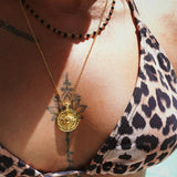 Person wearing a leopard print bikini top with a gold coin necklace featuring a compass pendant.