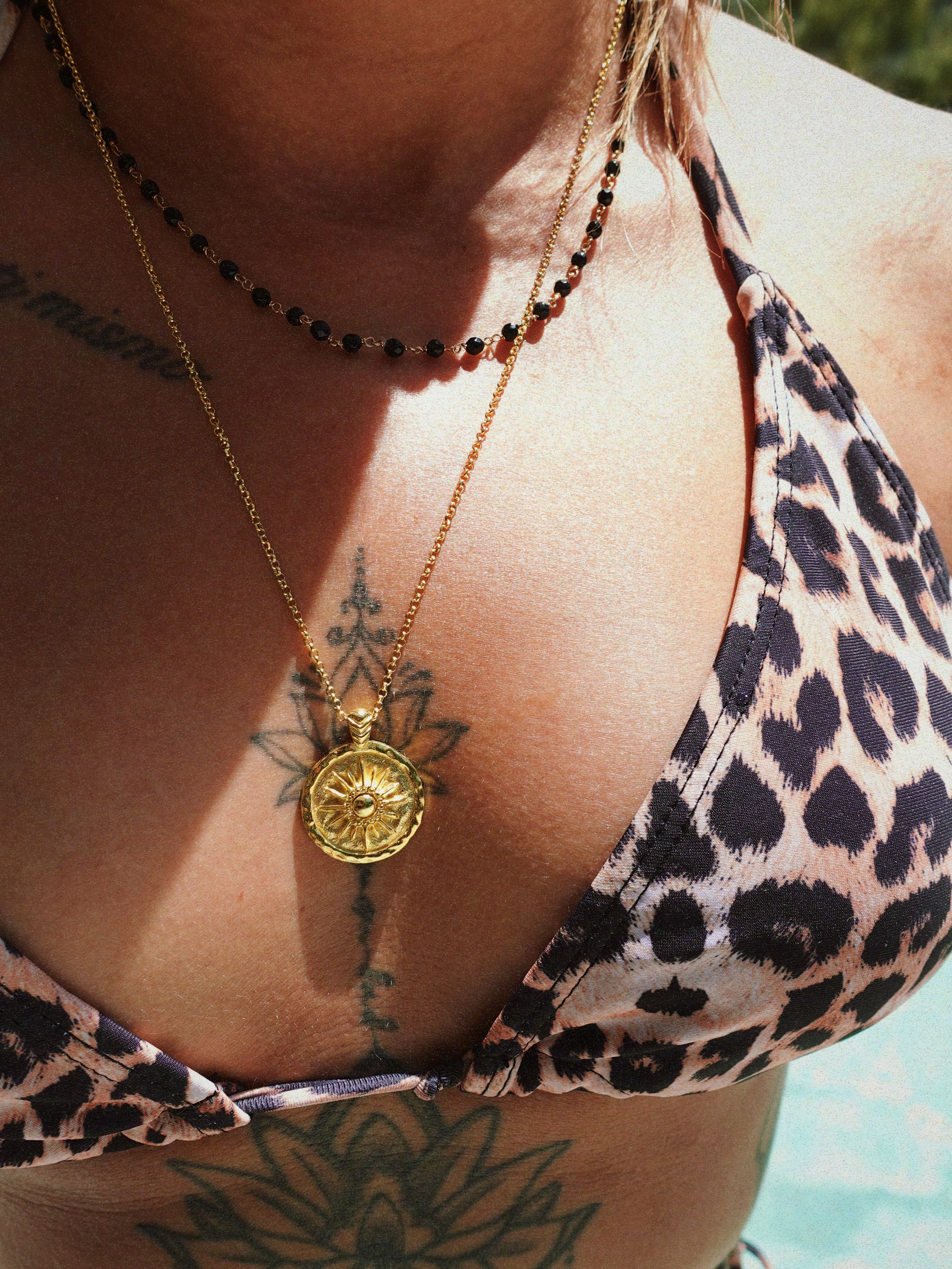 Person wearing a leopard print bikini top with a gold coin necklace featuring a compass pendant.
