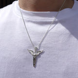 A silver pendant necklace featuring a stylized winged sword emblem on a chain, worn by a person wearing a white t-shirt.