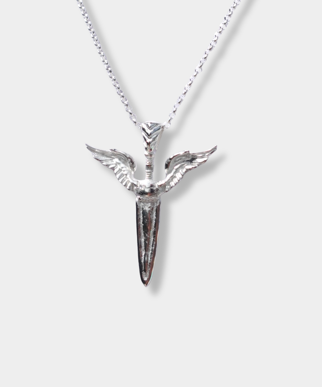 A silver pendant necklace featuring a dagger with wings, suspended from a delicate silver chain against a light gray background.