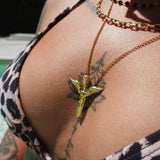 Close-up of a person wearing a gold necklace with a unique winged sword pendant, surrounded by tattoos.