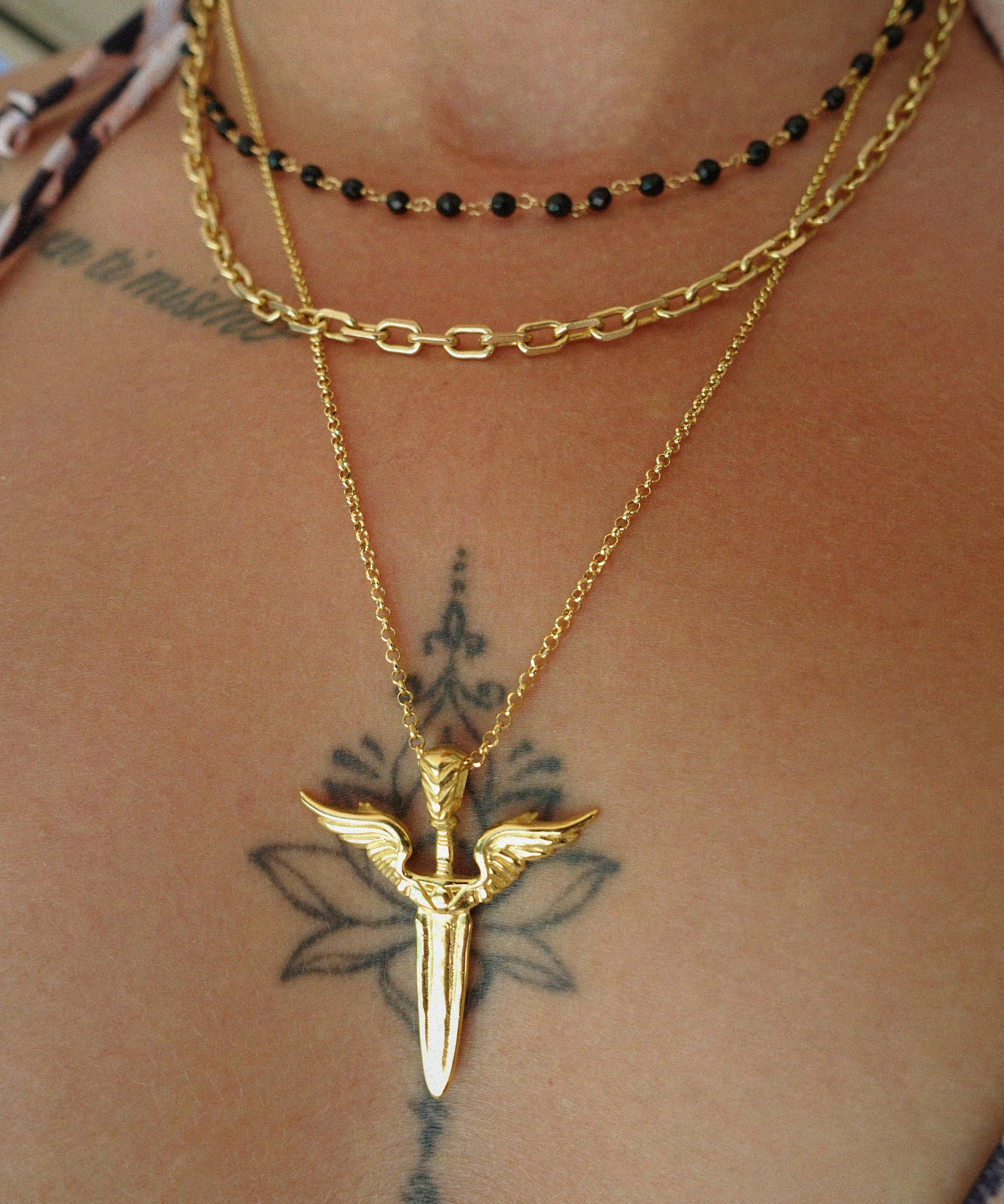 Gold necklace with a unique winged sword pendant on a person's neck with tattoos.