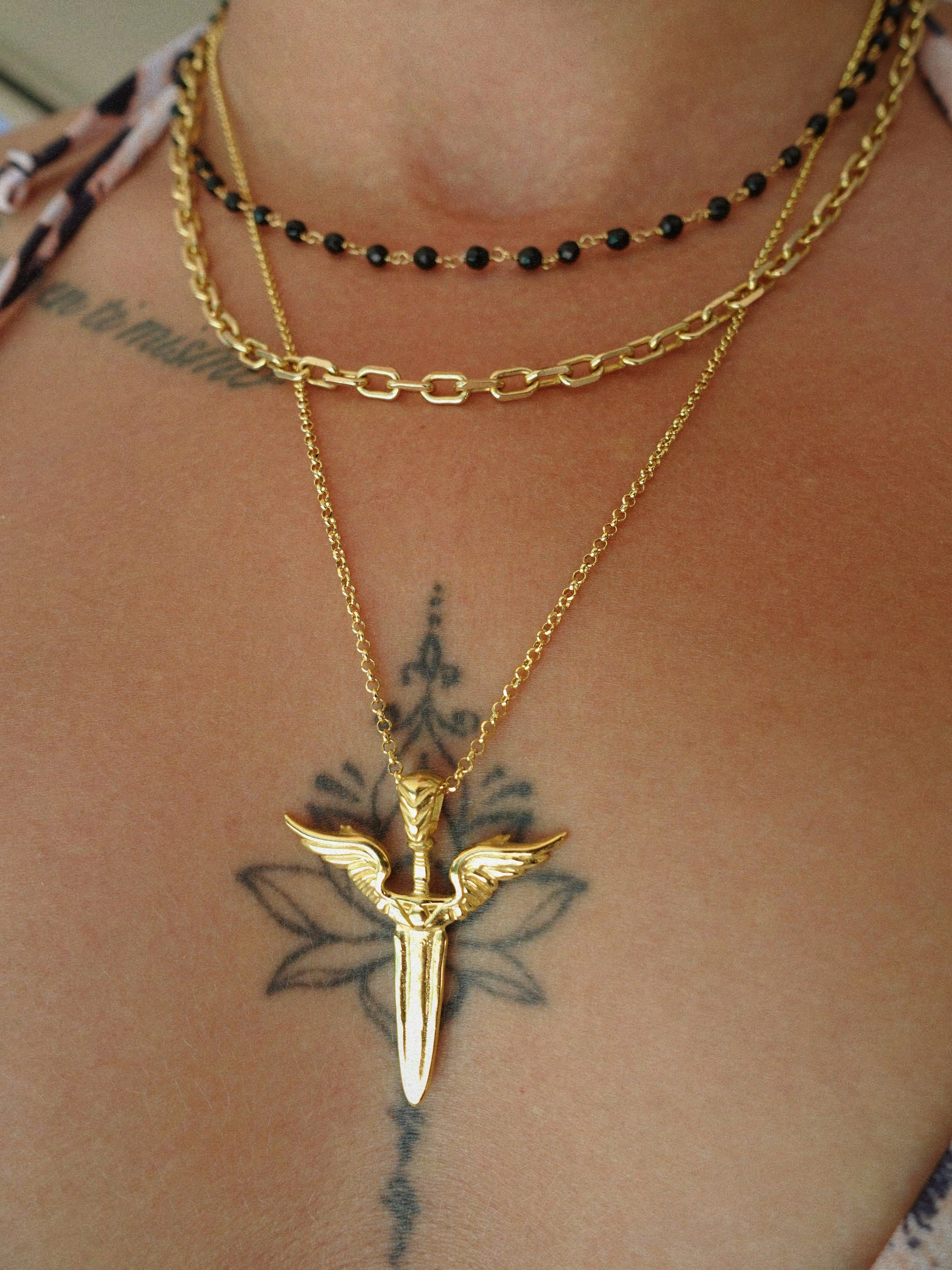 Gold necklace with a unique winged sword pendant on a person's neck with tattoos.