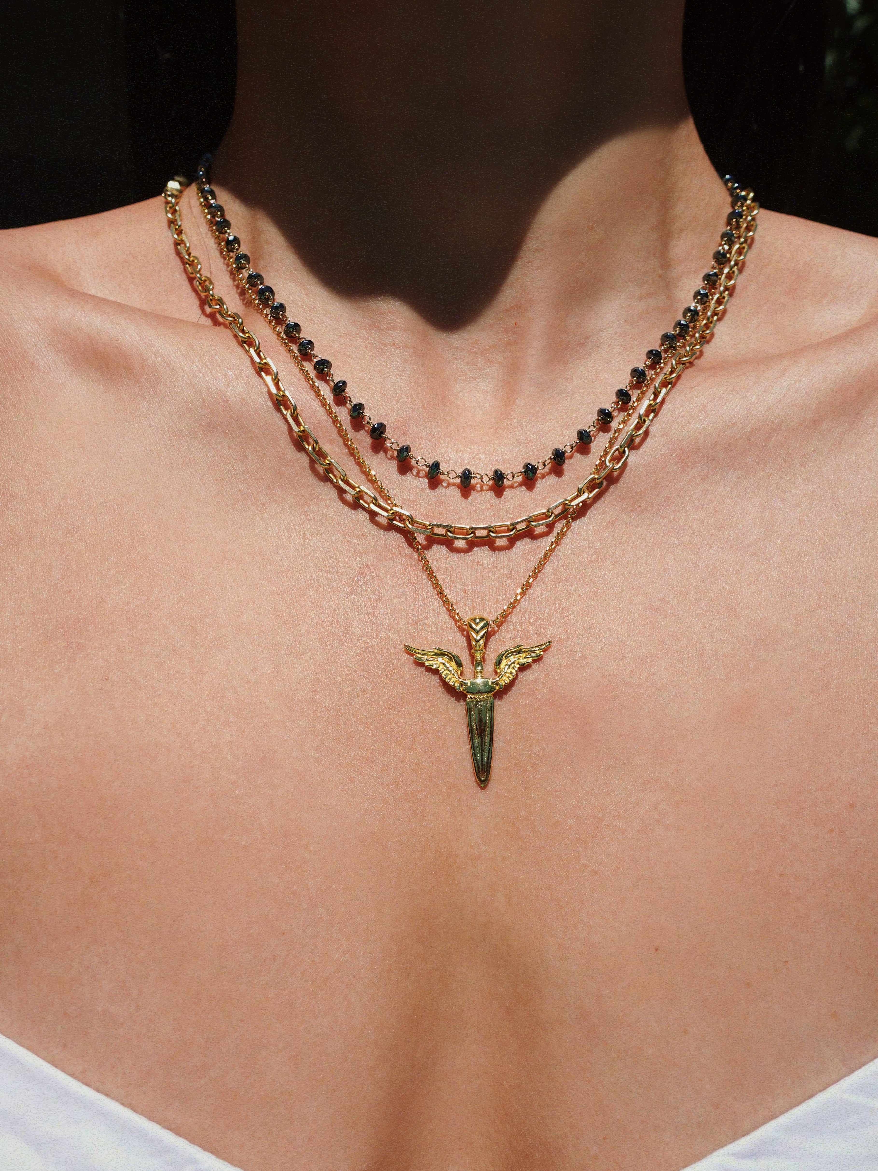 Necklace with a unique winged sword pendant on a person's neck