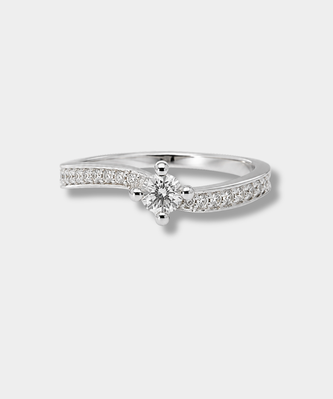 A silver-tone solitaire engagement ring with a round-cut center stone and pavé-set accent stones along the band, shown on a light gray background.