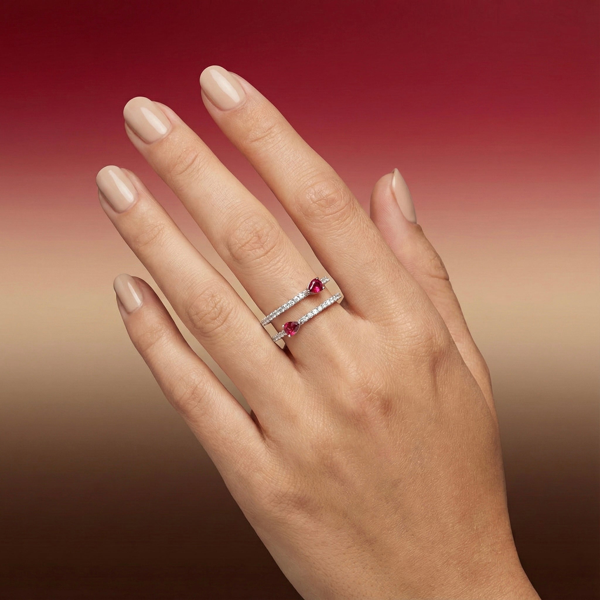 Hand wearing a diamond ring with red rubies against a gradient background