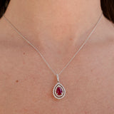 A white gold necklace with a teardrop-shaped pendant featuring a ruby gemstone on a person's neck.