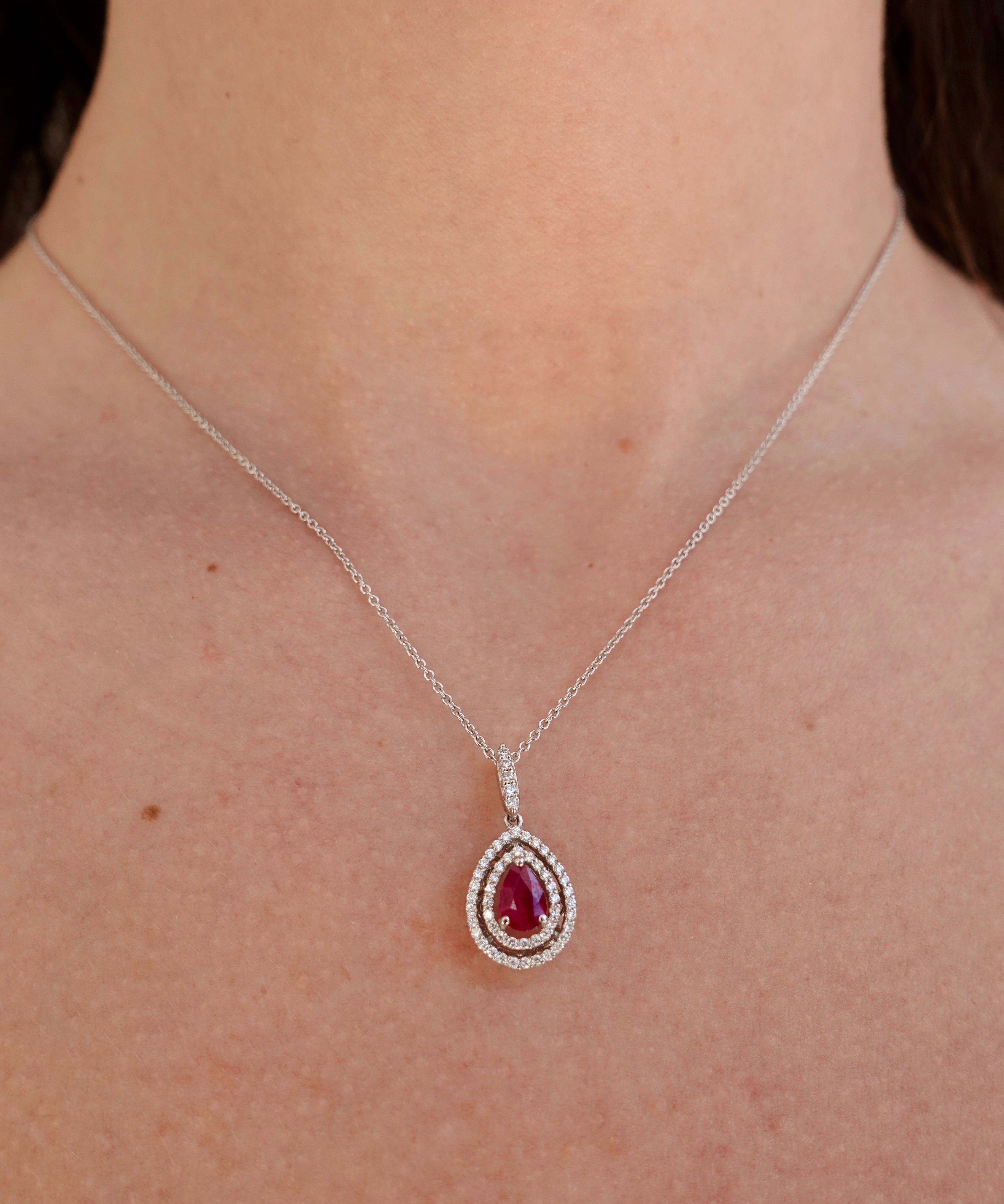 A white gold necklace with a teardrop-shaped pendant featuring a ruby gemstone on a person's neck.