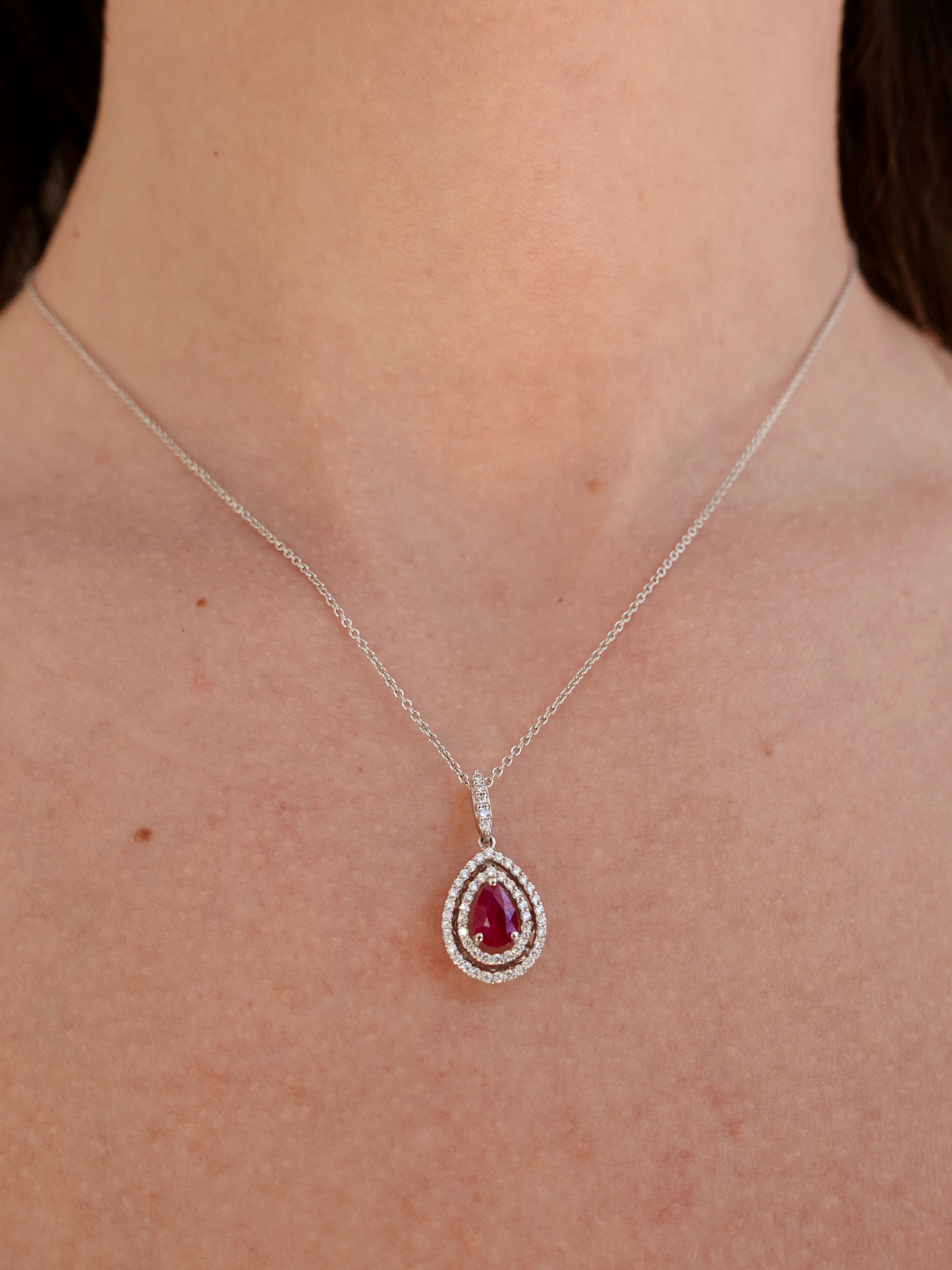 A white gold necklace with a teardrop-shaped pendant featuring a ruby gemstone on a person's neck.