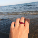 a hand wearing a ruby eternity ring over a background of sea waves
