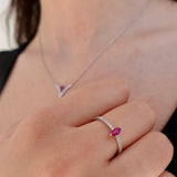 Close-up of a hand wearing a white-gold ring with a ruby gemstone, with a matching necklace in the background.