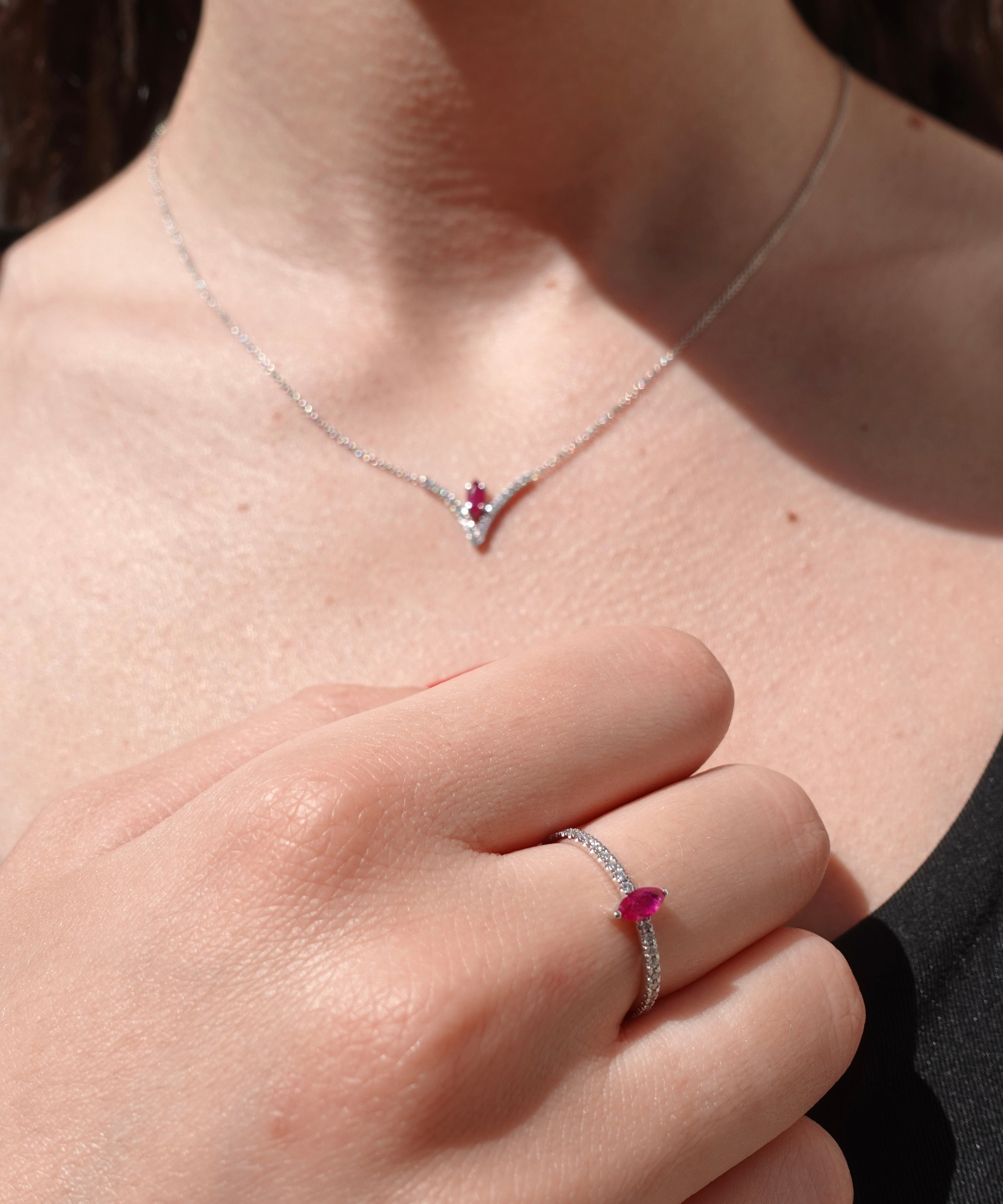 Close-up of a necklace and ring with ruby gemstones on a person's neck and hand.