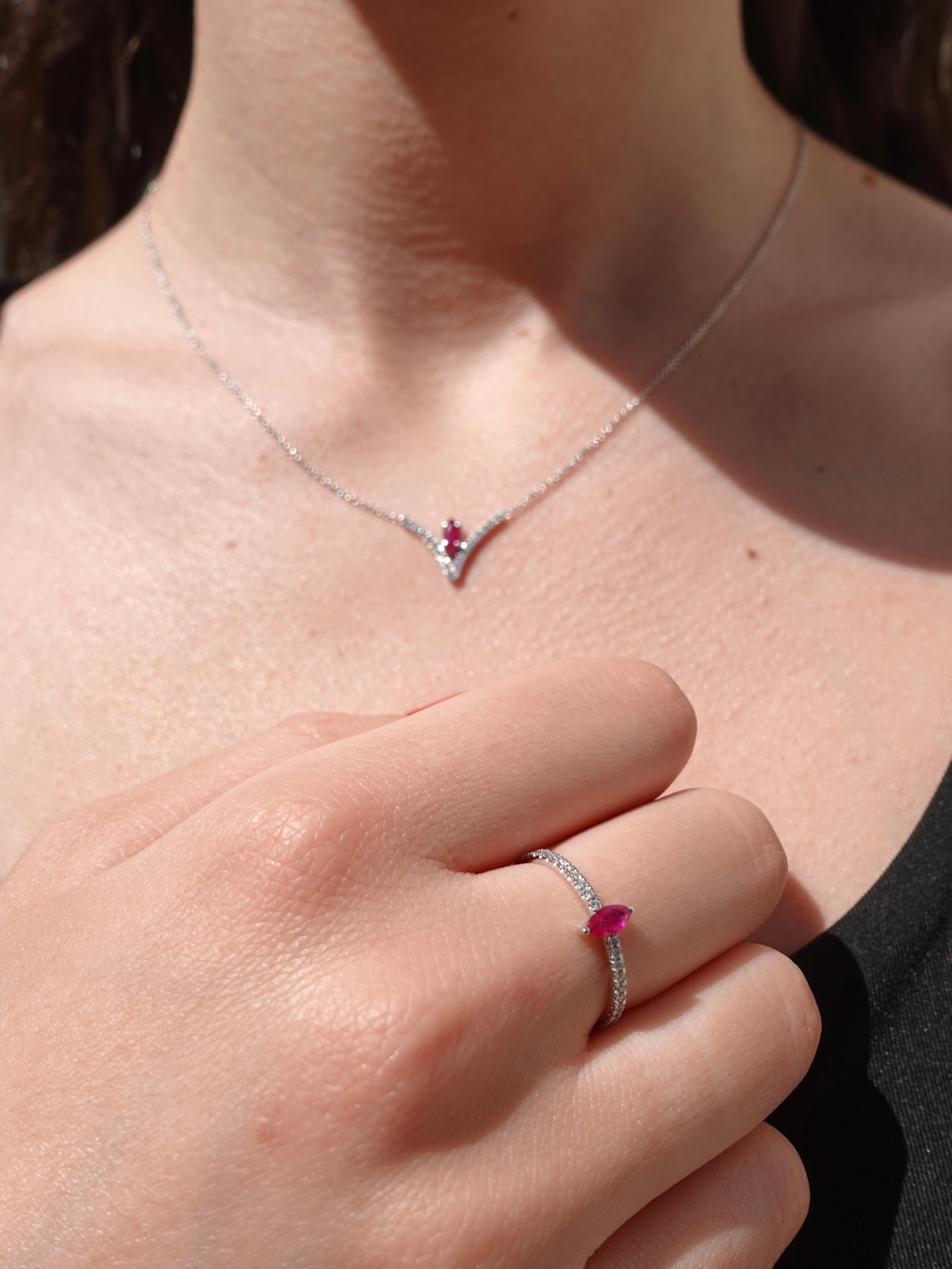 Close-up of a necklace and ring with ruby gemstones on a person's neck and hand.