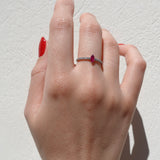 Hand wearing a ring with a red ruby gemstone on a light background