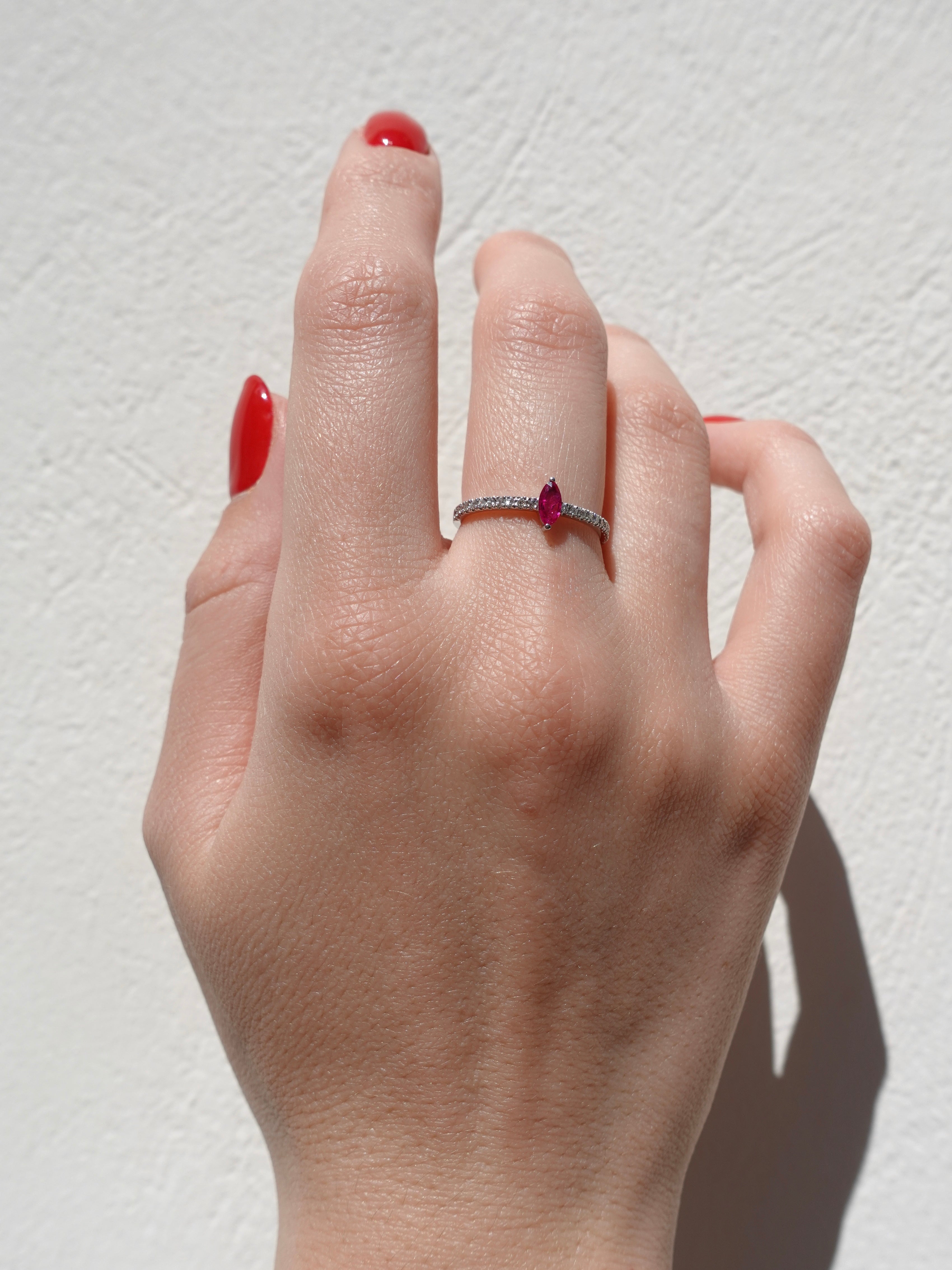 Hand wearing a ring with a red ruby gemstone on a light background