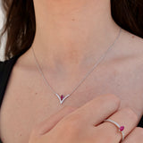 White gold necklace with a red gemstone worn by a person, with matching ring on a neutral background