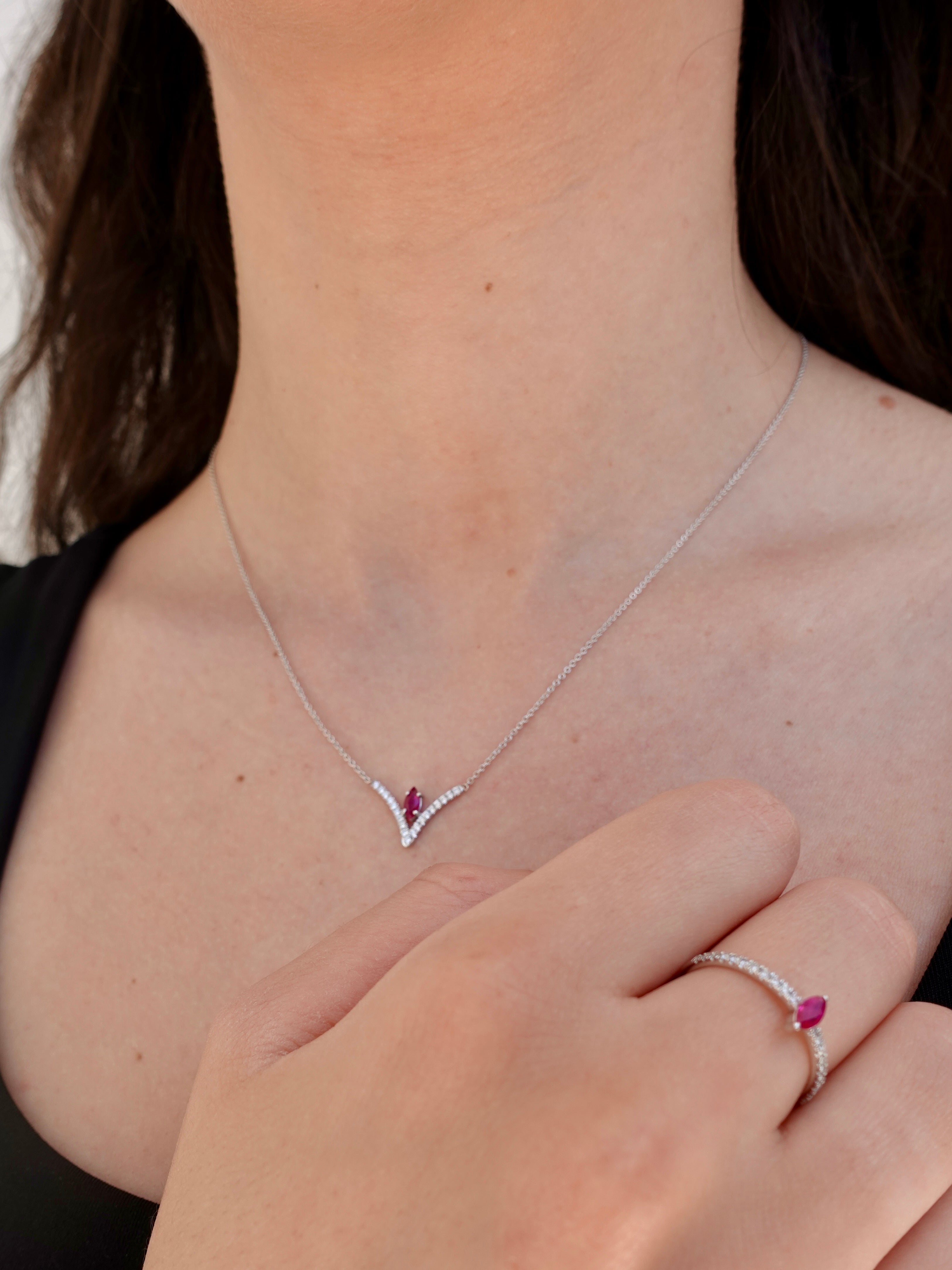 White gold necklace with a red gemstone worn by a person, with matching ring on a neutral background