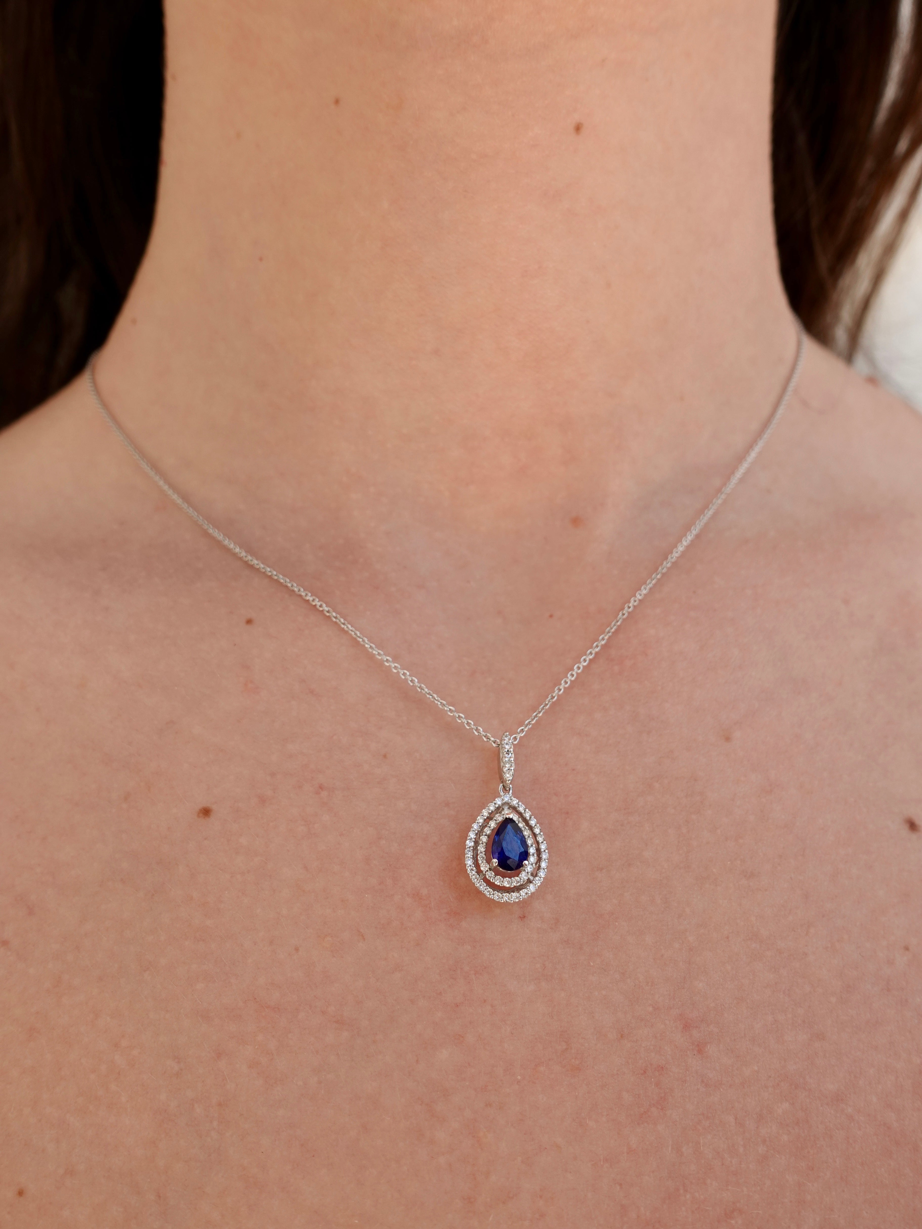 Necklace with a blue sapphire pendant worn by a person