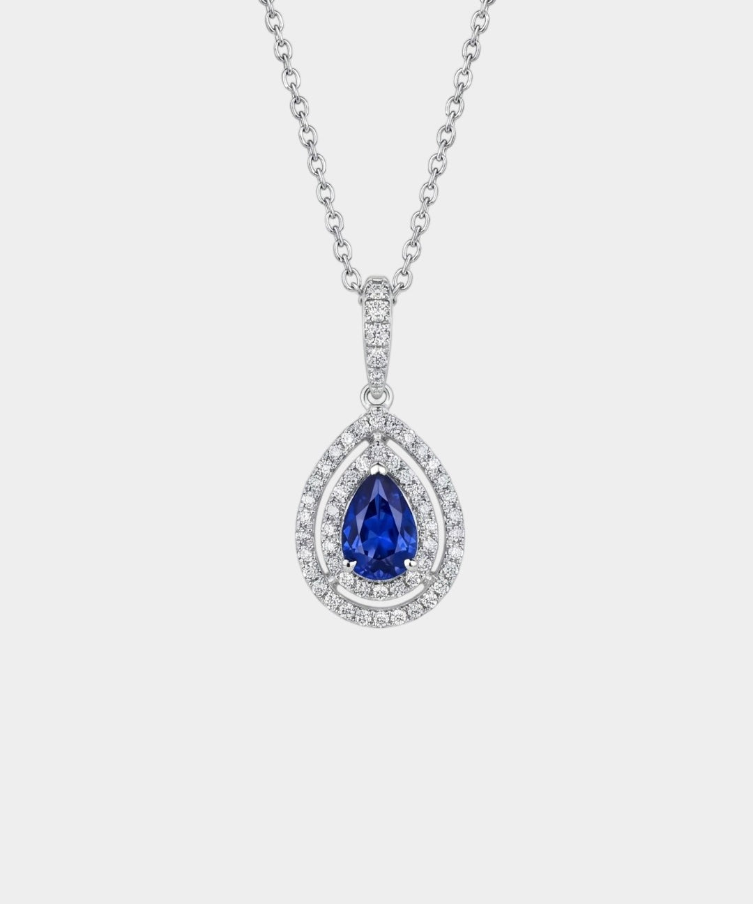 Gold necklace with a sapphire pendant and double diamond halo on a white background