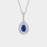 Gold necklace with a sapphire pendant and double diamond halo on a white background