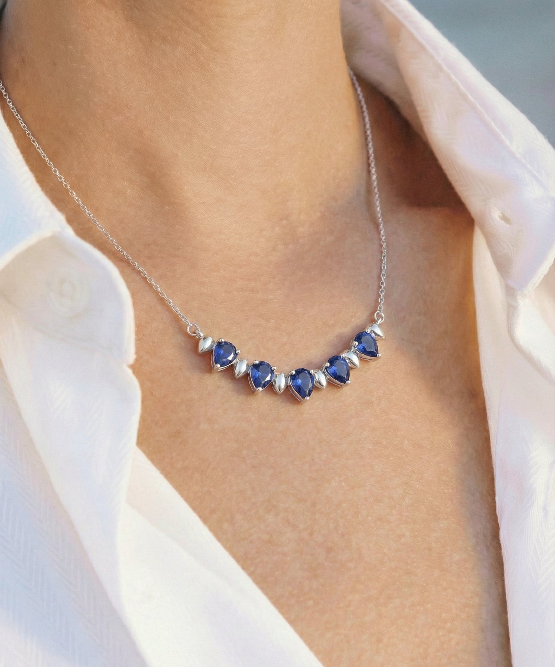 Necklace with blue sapphires worn by a person in a white shirt.