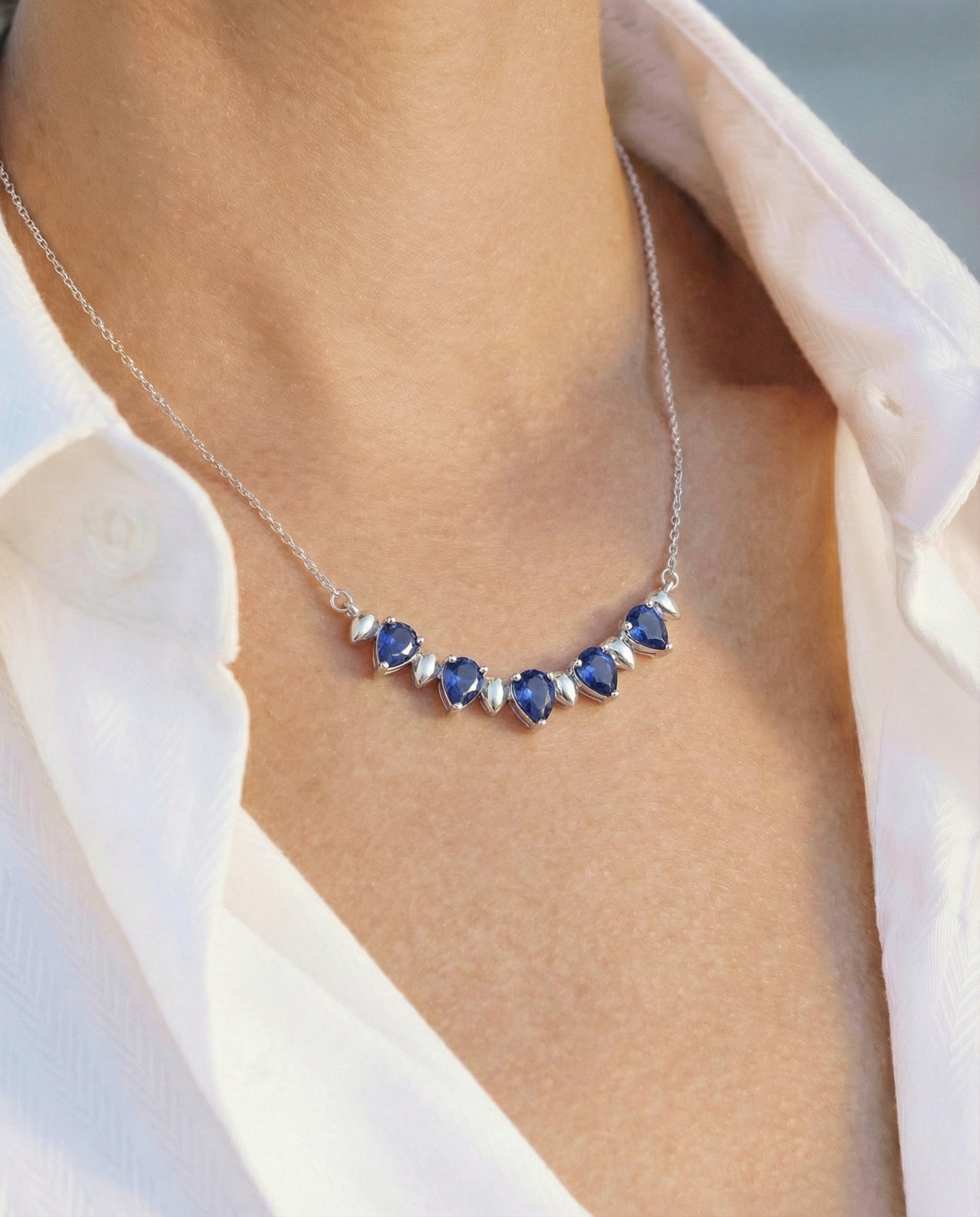 Necklace with blue sapphires worn by a person in a white shirt.