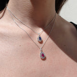 Close-up of a person wearing two white gold necklaces with gemstone pendants.