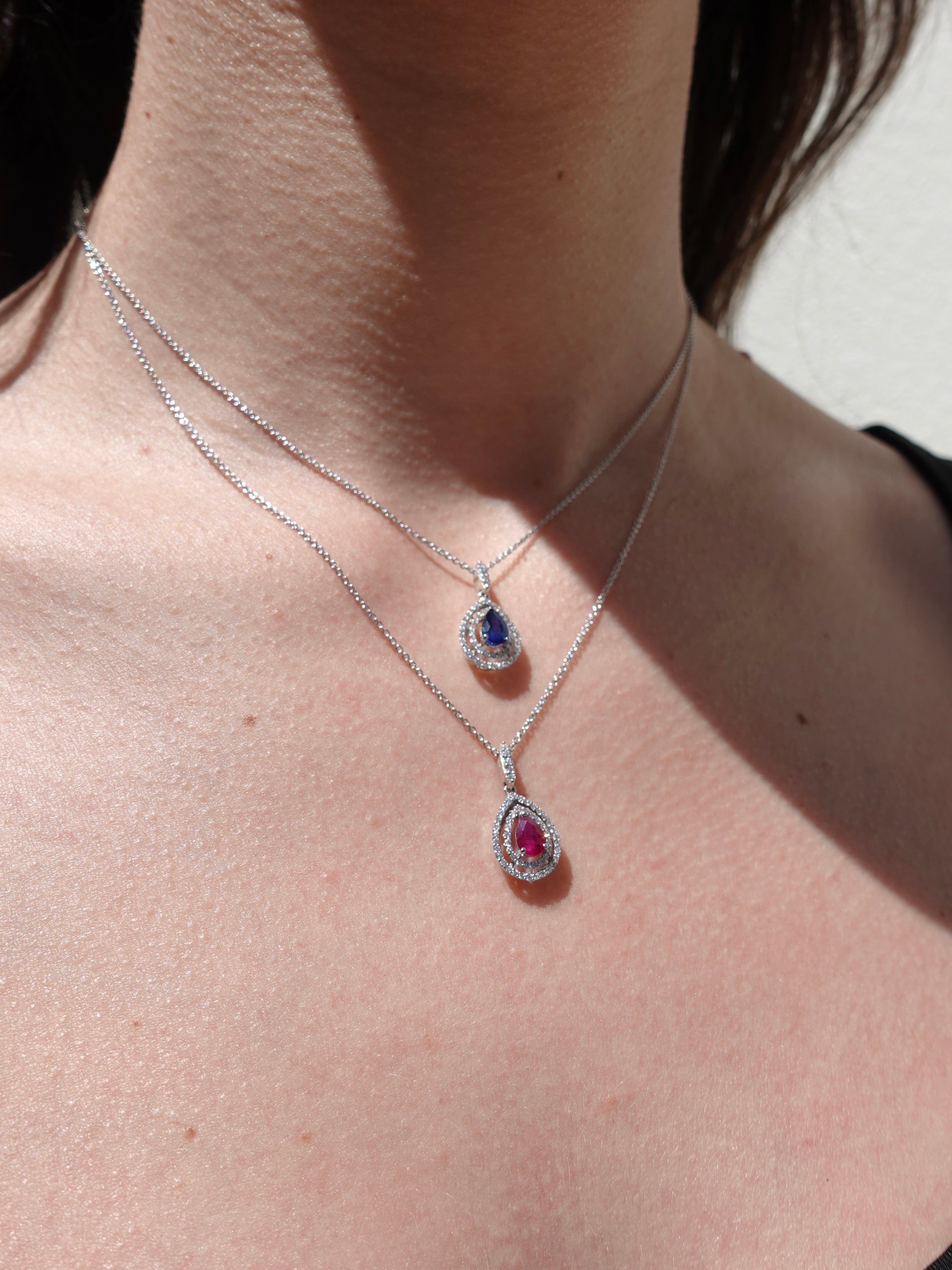 Close-up of a person wearing two white gold necklaces with gemstone pendants.