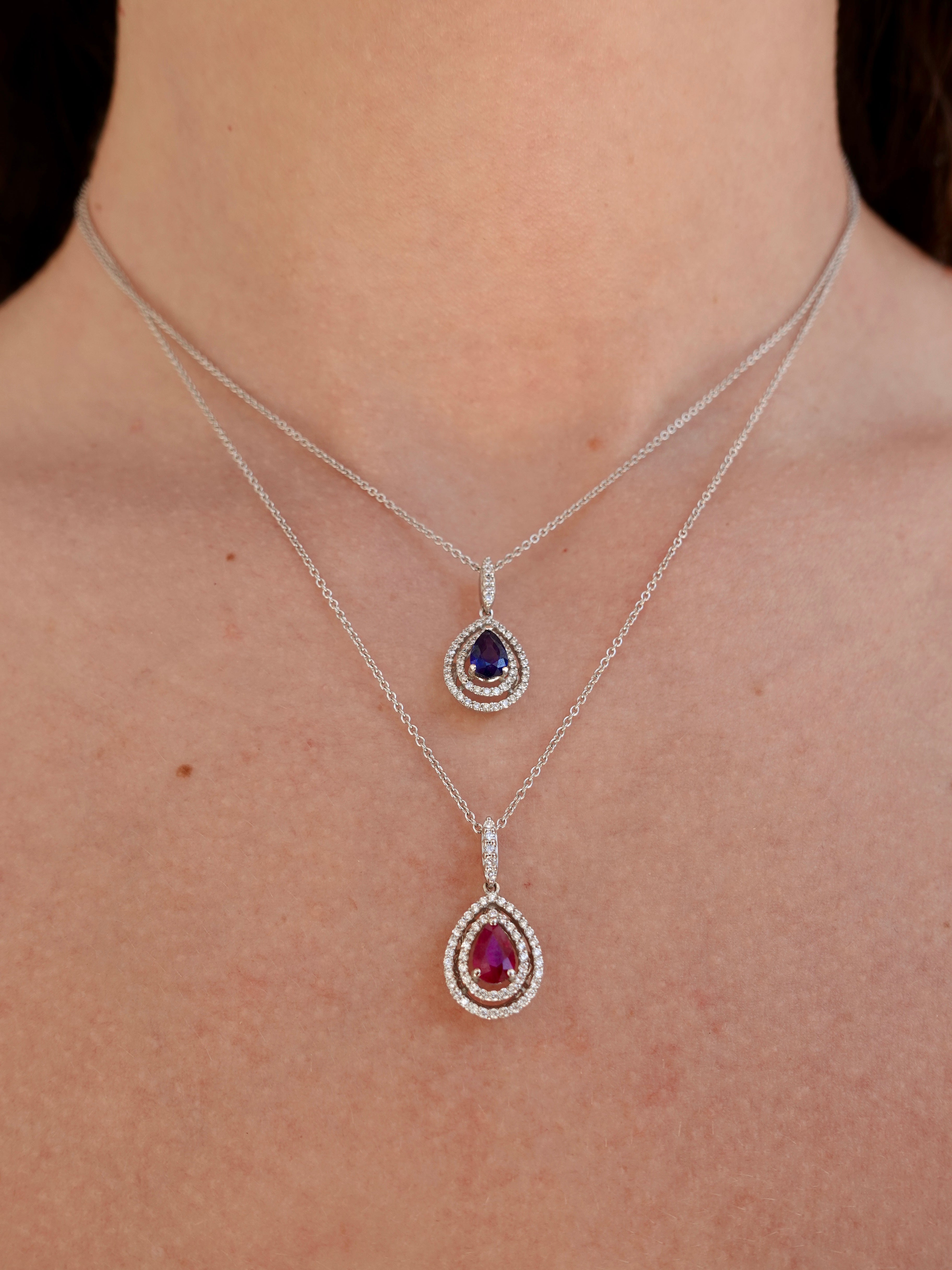 Two white-gold necklaces with gemstone pendants on a person's neck.