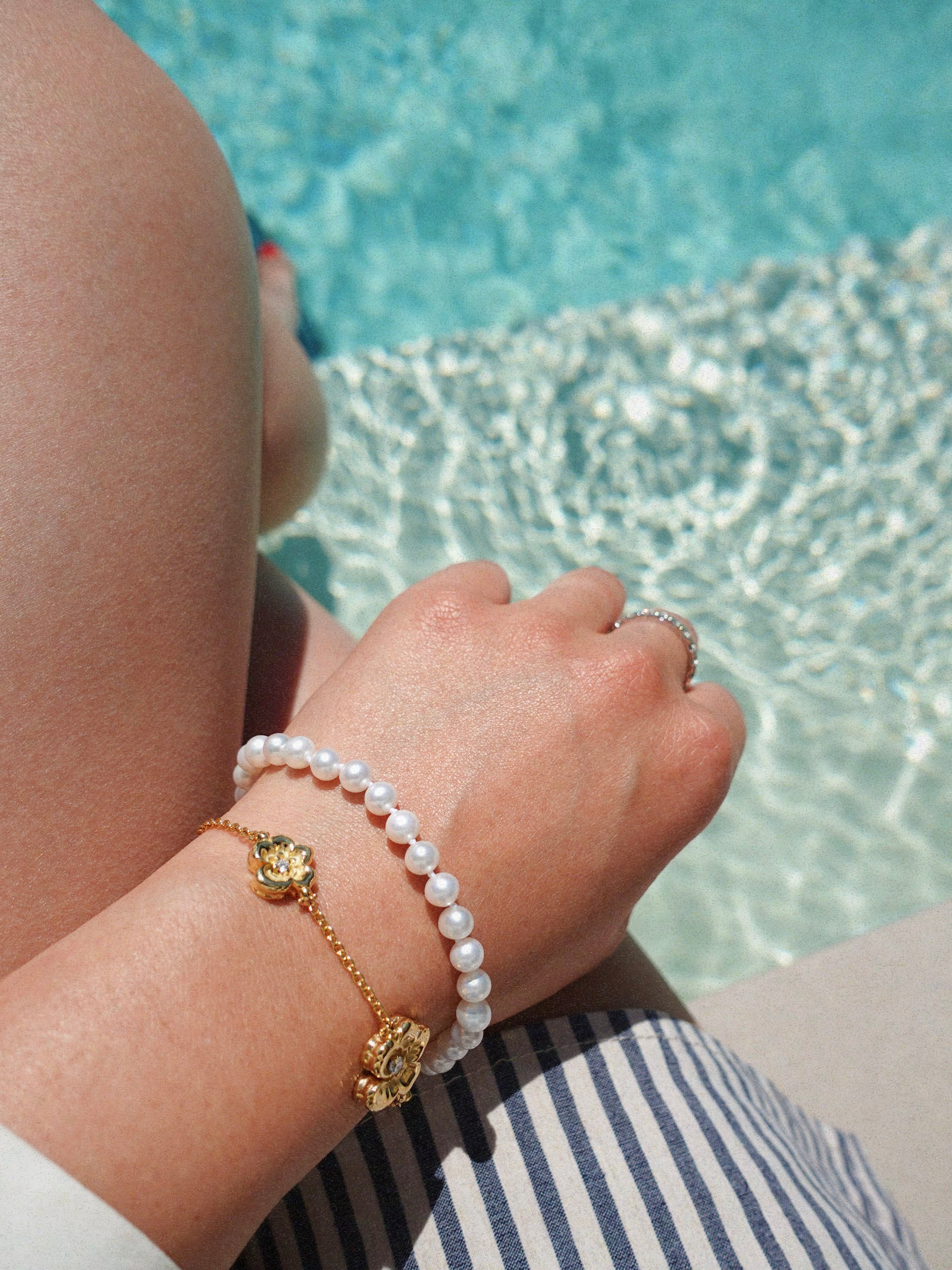Hand with pearl bracelet and gold flower charm by a pool