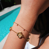 Gold bracelet with floral design on a person's wrist by a pool.