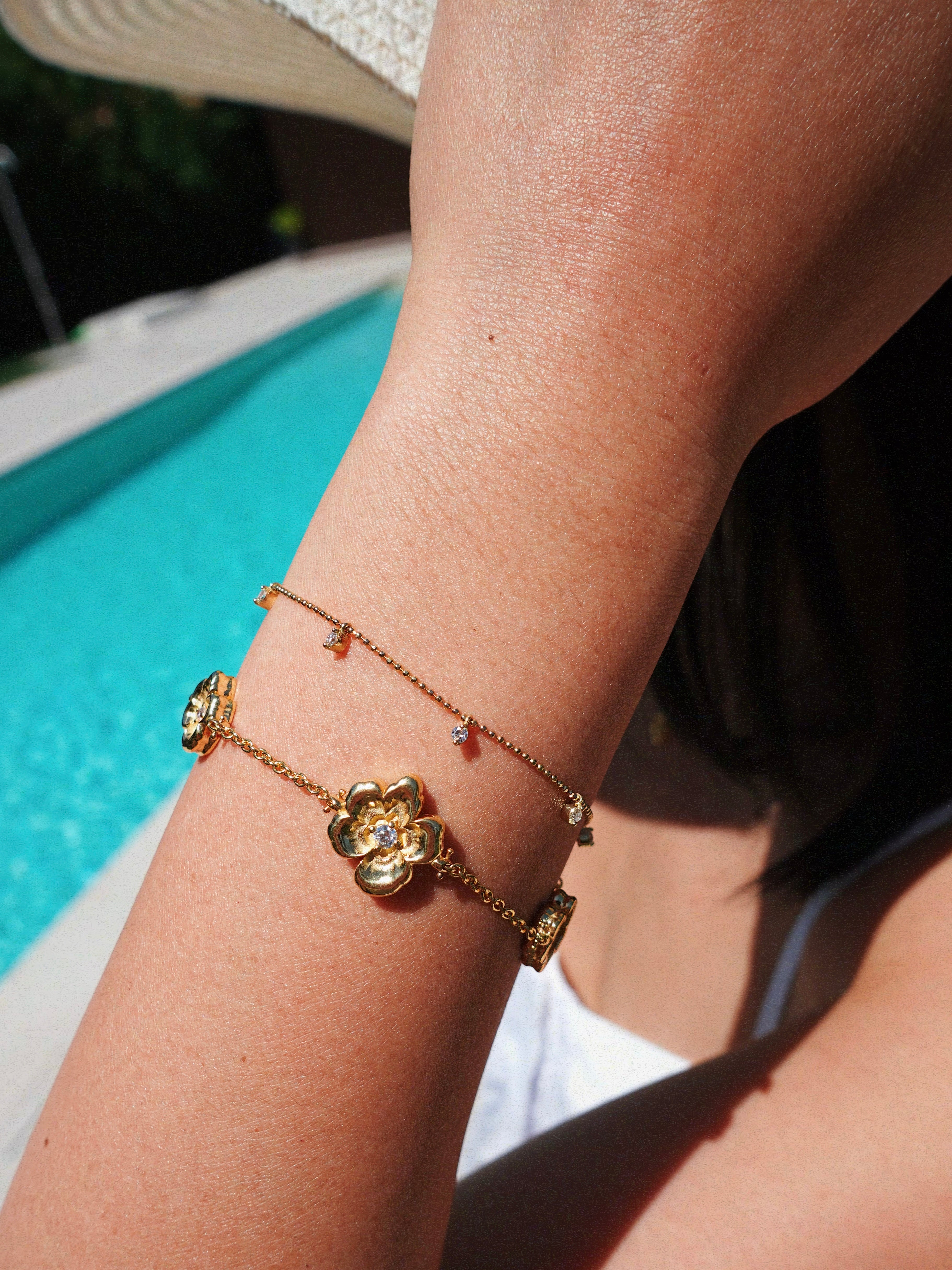 Gold bracelet with floral design on a person's wrist by a pool.